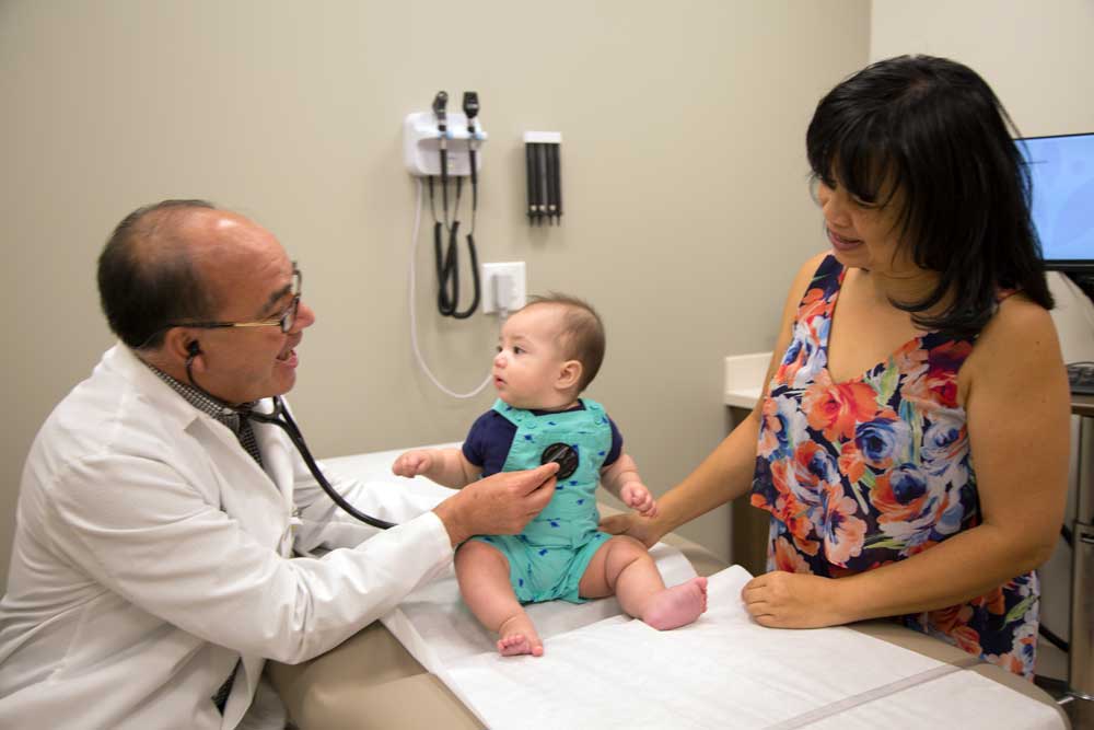 A doctor examining a baby with his mother watching